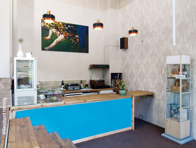 オリジナルの装飾モチーフが復元された壁面と、DDR時代の照明を使ったカフェ