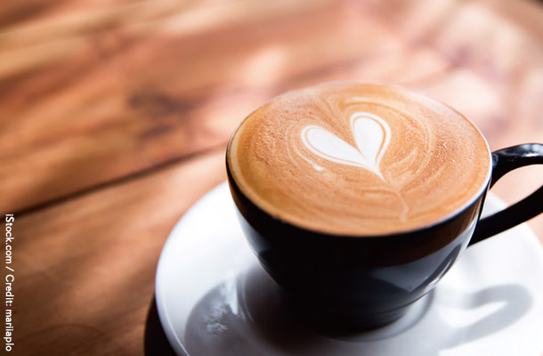 黒いコーヒーカップに入った白いハートのラテアートがついたカフェラテ